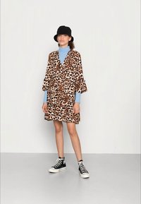 Jaqueta de padrão de leopardo com mangas plissadas, saia em camadas e gola alta azul. Usada com ténis de cano alto preto e branco.