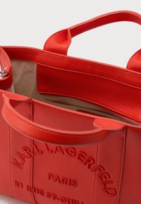 Geantă tote din piele texturată roșie, cu două mânere, un buzunar interior cu fermoar și inscripția "Karl Lagerfeld Paris" embosată pe față.