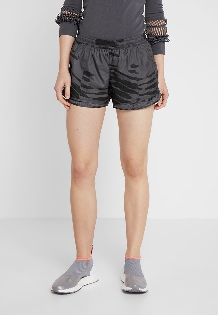 Svarta shorts med ett subtilt tigerrandigt mönster, elastisk midja och en avslappnad passform. Bärs med grå sportskor med meshdesign.