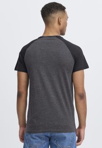 Camiseta de manga corta con diseño raglán negro, hecha de tejido gris oscuro. Presenta un cuello redondo y una textura suave.