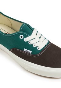 Canvas-Sneaker mit grünem Obermaterial und brauner Spitze, ausgestattet mit weißen Schnürsenkeln, Nähten und Branding. Gummisohle mit rutschfester Textur.