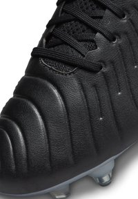 Schwarzer Fußballschuh mit strukturiertem Obermaterial, versehen mit gebogenen Rillen, schwarzen Schnürsenkeln und transparenten Stollen für besseren Halt.