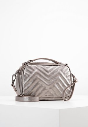 Metallisk sølv crossbody-taske med chevron-quiltet mønster, lynlåslukning, tophåndtag og aftagelig rem på hvid overflade.