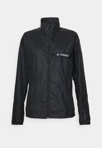 Chaqueta cortavientos ligera negra Adidas Terrex con cremallera frontal y cuello alto, diseñada para actividades al aire libre.