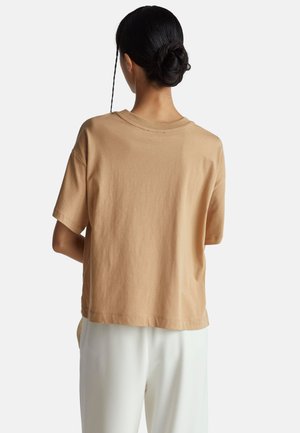 Béžové bavlněné tričko s volnějším střihem, krátkými rukávy a kulatým výstřihem. Zadní pohled ukazuje hladkou texturu a jednoduchý design.