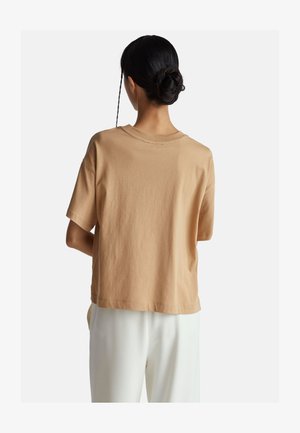 Beżowa bawełniana koszulka z luźnym krojem, krótkimi rękawami i okrągłym dekoltem. Widok z tyłu ukazuje gładką teksturę i prosty design.