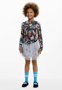 Langærmet sort skjorte med farverige grafikker; lagdelt hvid tylskørt; blå knæstrømper med hvide striber; sorte sko.