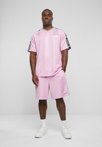 Pink athletic short-sleeve shirt and shorts set, featuring black logo accents and a V-neck design, made from smooth synthetic fabric.