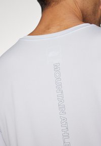 White athletic shirt with short sleeves. Features a soft, textured fabric and a vertical "MOUNTAIN ATHLETE" logo on the back in light gray.