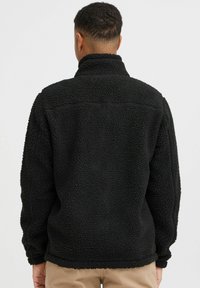 Black fleece pullover featuring a high collar, soft texture, and a relaxed fit. Seam details are visible along the shoulders.