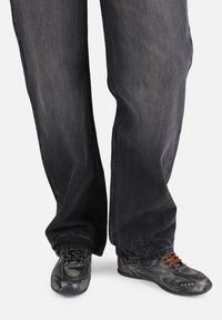 Svarte denimbukser med løs passform, kombinert med svarte sneakers som har et teksturert design og brune snøringer.
