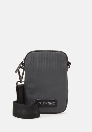 Sac en nylon noir à bandoulière avec fermeture à glissière, présentant une surface texturée, une sangle détachable, et un accent logo sur le devant.