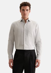 Lys grå skjorte med knaplukning lavet af et tekstureret stof, som har en brystlomme og klassisk krave, parret med sorte bukser.