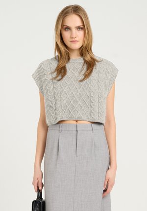 Šedý pletený cropped top s texturovaným kabelovým designem, s širokými rukávy. V kombinaci se šedou přizpůsobenou tužkovou sukní a černou kabelkou.
