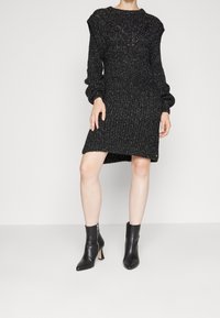 Robe pull noire en tricot avec un tissu texturé, longues manches bouffantes et ourlet côtelé, assortie à des bottines noires à bout pointu.