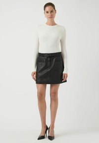 Svart skinnskjørt med frontplisseringer, to sidelommer og belte i midjen. Kombinert med en tettsittende hvit langermet topp.