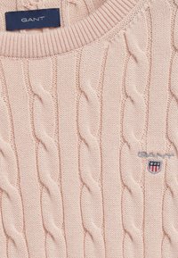 Jasnoróżowy sweter z dzianiny o splocie warkoczowym, z ribbowanym dekoltem, ozdobiony wyhaftowanym logo oraz subtelnym wzorem teksturowym.