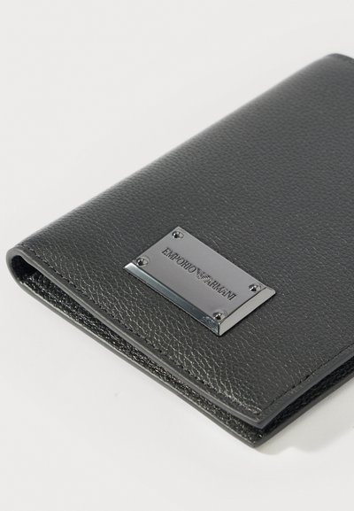 Μαύρο πορτοφόλι από δερμάτινη υφή με ασημένια πινακίδα με το λογότυπο Emporio Armani στην πρόσοψη, τοποθετημένο σε γωνία σε λευκό φόντο.