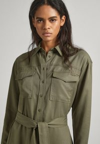 Vestito camicia khaki con maniche lunghe, chiusura con bottoni, due taschini sul petto e vita con cintura. Tessuto morbido con vestibilità comoda e colletto classico.