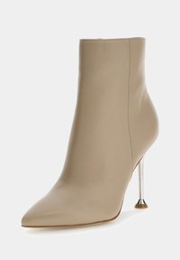 Bota de tobillo de cuero beige con punta afilada, textura suave y delgado tacón de stiletto metálico, con un acento redondeado en la base.