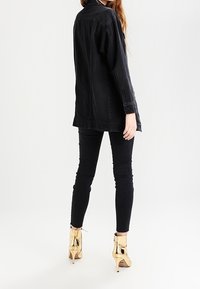 Svart denimjacka med avslappnad passform, kombinerad med svarta skinny jeans och guldiga ankelboots. Funktioner inkluderar långa ärmar och en krage.