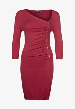 Punainen neulemekko, jossa on V-pääntie, kolmivartiset hihat, sivuruuska ja viisi koristepainiketta vasemmalla puolella. Tasainen rakenne.