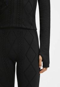 Czarny sportowy zestaw składający się z teksturowanego długiego rękawa z wzorem diamentu oraz dopasowanych legginsów z wysokim stanem.