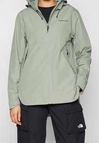 Giacca impermeabile verde chiaro con zip frontale, cappuccio regolabile e tasche laterali. Presenta un logo distintivo sul petto e sui polsini.