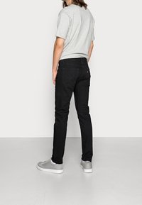 Svarta jeans med en åtsittande design, med bakfickor och en liten röd logotagg. I kombination med en grå t-shirt och grå sneakers.