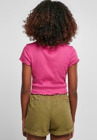 Krótki różowy crop top o prążkowanej fakturze i falbaniaste krawędzie, zestawiony z oliwkowo zielonymi szortami z mankietami i tylnymi kieszeniami.