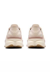 Zapatillas deportivas de color rosa claro y beige con material liso, forma redondeada en la parte trasera, detalles elevados y suela blanca con agarre texturizado.