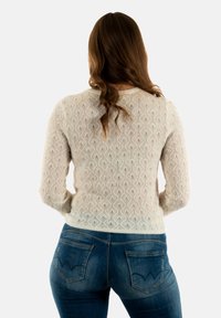Maglione in cotone beige chiaro con motivo a diamante, maniche lunghe e orlo a costine, abbinato a jeans in denim blu medio con dettagli delle tasche curvi.