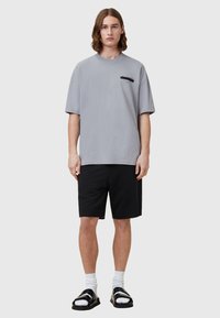 T-shirt en coton gris à manches courtes, avec un petit logo noir sur la poitrine, associé à un short noir et des sandales.