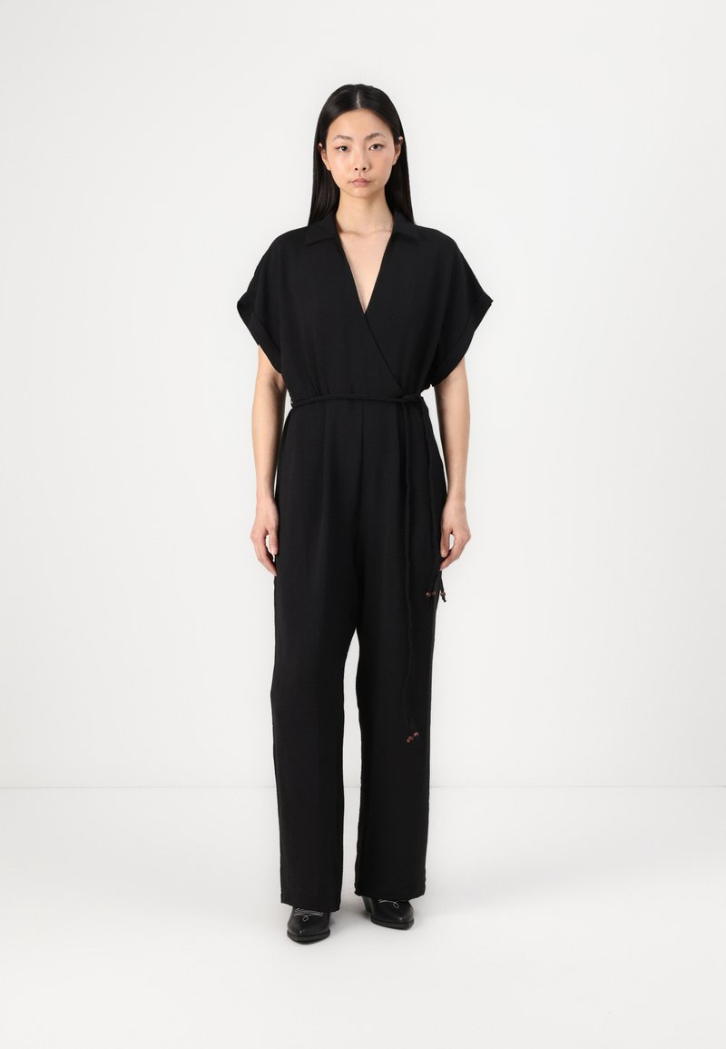 Svart jumpsuit med v-hals og korte ermer, innsnurt i livet med et belte; har teksturert stoff og vide bukser.