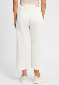 Pantalons larges blancs en coton, avec une taille haute, deux poches arrière et un accent beige à la taille. Associés à des baskets claires.