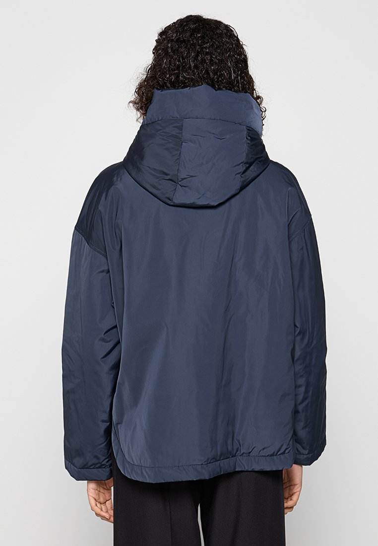Marineblauwe, gewatteerde jas met een capuchon, met een glad, glanzend oppervlak en een elastische zoom. Eenvoudig ontwerp zonder zichtbare versieringen.