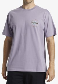 Camiseta de algodón lavanda con un logo multicolor en el pecho. Mangas cortas y un corte relajado. Textura suave.