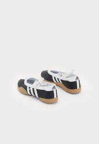 Black and white athletic shoes with a gum rubber sole, lace-up design, and three white stripes on the side. Smooth material with a rounded shape.