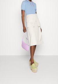 Light blue ribbed knit top with pink trim, cream knee-length skirt with front pockets, lavender handbag, and green platform clogs.