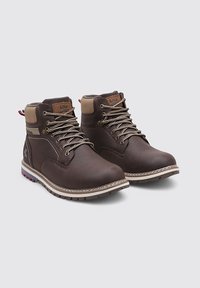 Un par de botas de cuero marrón con cordones hasta el tobillo, con cuellos acolchados beige y suelas de goma, expuestas sobre un fondo gris.