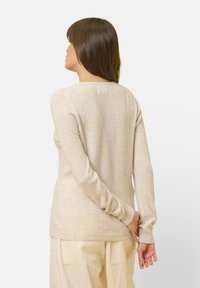 Maglione beige a maniche lunghe con una texture morbida e polsini a coste. Presenta un collo rotondo e una vestibilità leggermente rilassata.