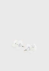 Brincos de pressão transparentes com hastes em metal prateado. Apoio circular em plástico transparente. Pequenos detalhes decorativos na superfície frontal.