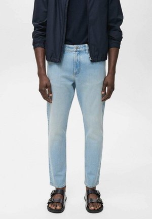 Lichtblauwe denim jeans, slim fit, licht beschadigd met zichtbare stiksels, gecombineerd met zwarte sandalen en een marineblauwe jas.