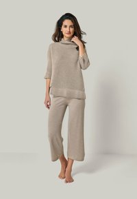 Beige Strickpullover mit einem Kragen und Dreiviertelärmeln, kombiniert mit weit geschnittenen passenden Hosen, beide mit einer strukturierten Oberfläche.