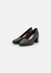 Scarpe con tacco alto in pelle nera con punta arrotondata e tacco medio a blocco, caratterizzate da una texture liscia e un design minimale.