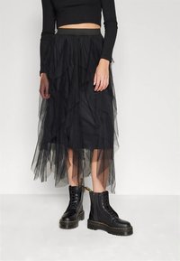 Črna večplastna tila krilo z elastičnim pasom, z nagubanimi plastmi. Oblečeno s črnimi škornji z vezalkami in debelim podplatom.