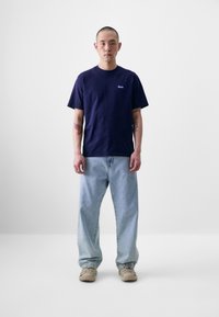 Tricou din bumbac de culoare albastru marin, cu guler rotund, mâneci scurte, asociat cu blugi din denim de culoare albastru deschis cu croială lejeră și adidași bej cu finisaj texturat.