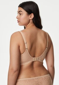Sujetador de encaje beige con tirantes ajustables, patrón floral y cierre en la parte posterior. Textura suave con detalles sutiles y un ajuste cómodo.