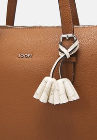 Sac à main en cuir marron texturé avec des accessoires en métal argenté. Comprend une frange en cuir blanc avec un motif gravé et un embellissement de logo.