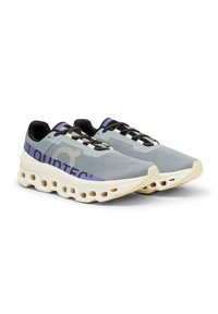 Baskets de sport légères en gris et crème avec des lacets noirs, dotées d'une semelle moulée distinctive avec de grandes découpes et des accents de marque violets.